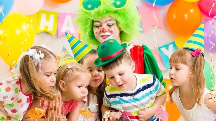 children with clown celebrating birthday party and blowing candle on cake